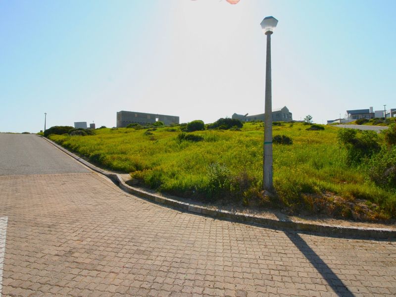 A view of a vacant residential plot from the street, featuring paved access, concrete curbing, and established street lighting.