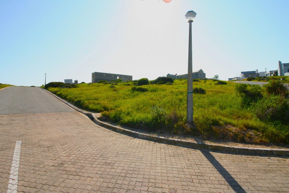 A view of a vacant residential plot from the street, featuring paved access, concrete curbing, and established street lighting.