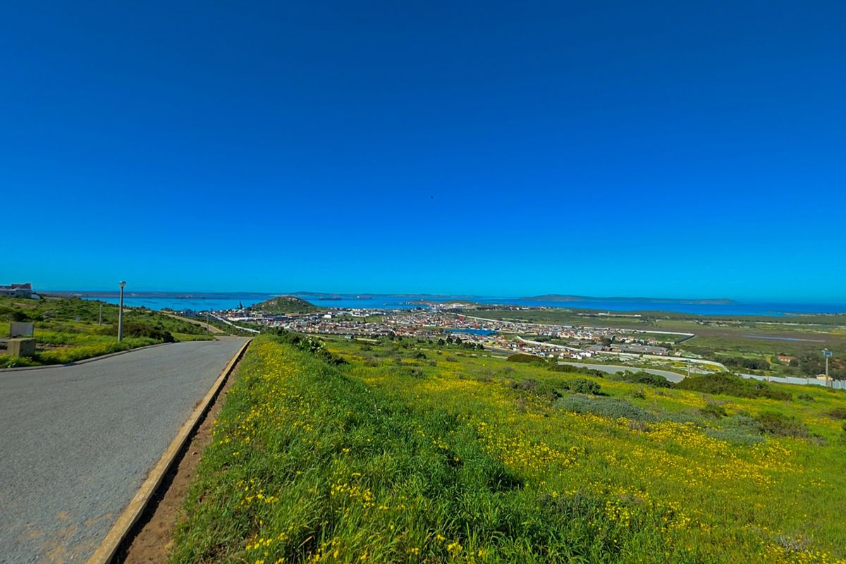 A scenic elevated view overlooking the coastal town and surrounding landscape, featuring a paved access road in the foreground.