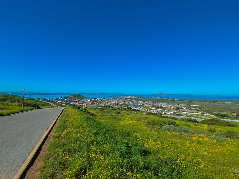 A scenic elevated view overlooking the coastal town and surrounding landscape, featuring a paved access road in the foreground.
