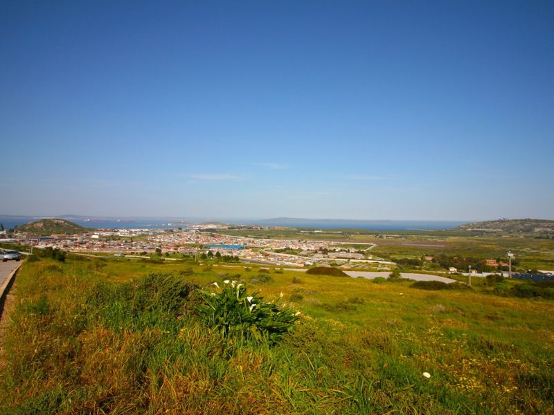 A wide-angle view overlooking the surrounding landscape, residential area, and distant coastline from the vacant land plot.