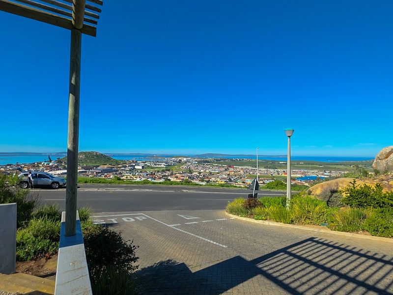 A scenic elevated view overlooking the surrounding town and coastline, featuring a paved driveway and timber pergola structure in the foreground.