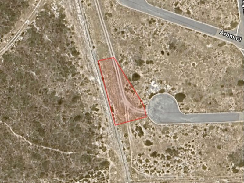 An aerial view of a vacant residential plot outlined in red, showing the surrounding landscape and nearby road access.