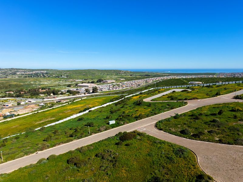 An aerial view of a vacant residential land plot featuring established paved roads and perimeter fencing, overlooking the surrounding coastal landscape.