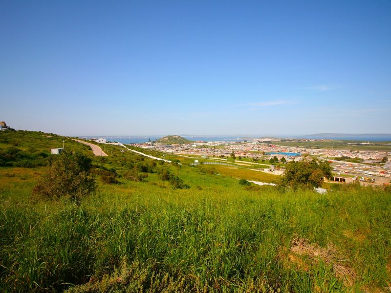 A scenic elevated view overlooking the surrounding residential landscape, coastal area, and distant hills, showcasing the natural terrain of the vacant land.