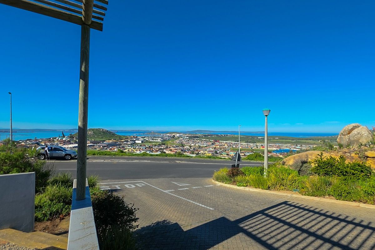 A scenic elevated view overlooking the surrounding town and coastline, featuring a paved driveway and timber pergola structure in the foreground.