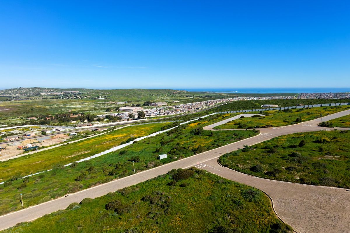 An aerial view of a vacant residential land plot featuring established paved roads and perimeter fencing, overlooking the surrounding coastal landscape.