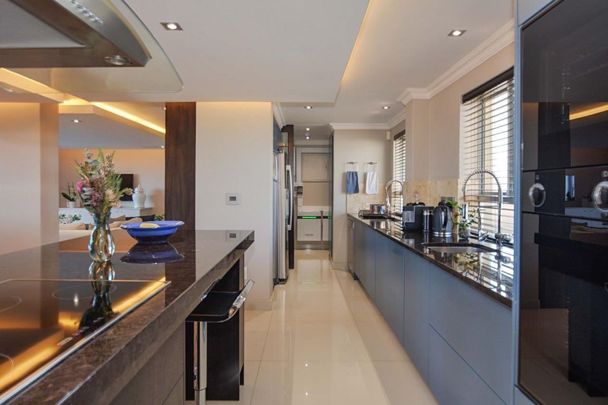 Modern kitchen featuring sleek dark cabinetry, granite countertops, integrated appliances, and high-quality finishes with recessed and cove lighting.