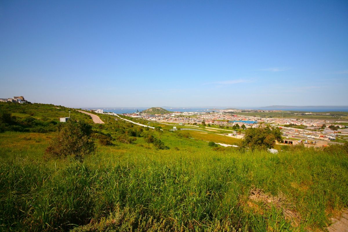 A scenic elevated view overlooking the surrounding residential landscape, coastal area, and distant hills, showcasing the natural terrain of the vacant land.