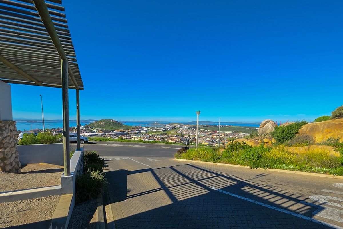 Elevated view overlooking the town and coastline, featuring a paved driveway and a wooden pergola structure in the foreground.