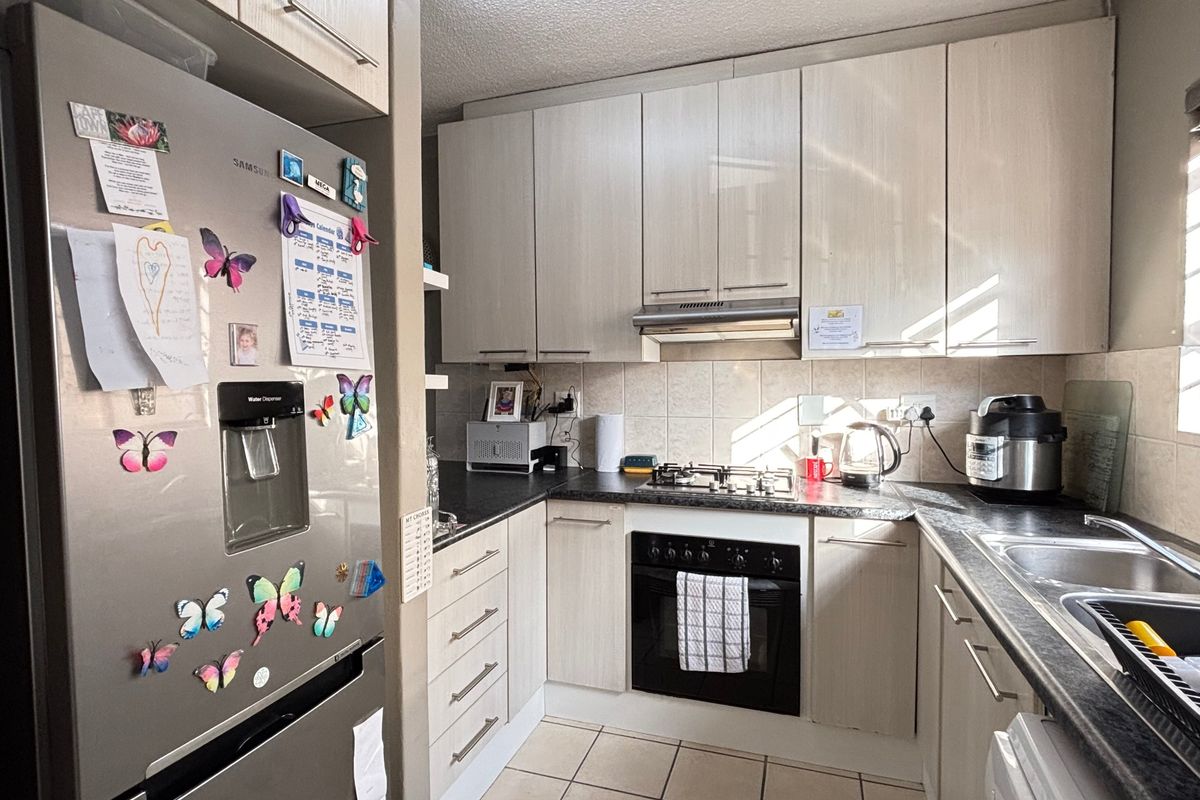 A functional kitchen featuring light-toned cabinetry, dark countertops, a gas hob, built-in oven, and tiled flooring.