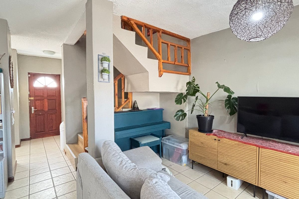 Open-plan living area featuring a staircase with a wooden balustrade, tiled flooring, and direct access to the front entrance.
