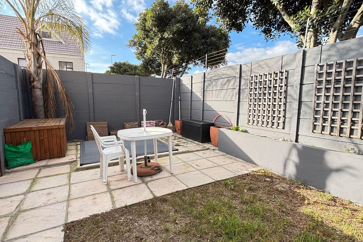 A private rear courtyard featuring a paved patio area, raised planter boxes, and secure boundary walls with electric fencing.