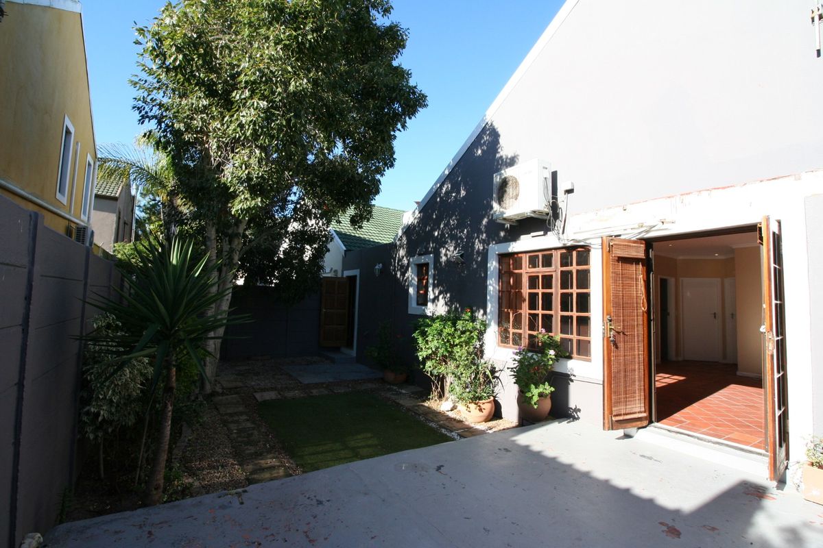 Rear exterior view featuring a paved patio area, small garden space, and direct access to the interior through timber framed doors.