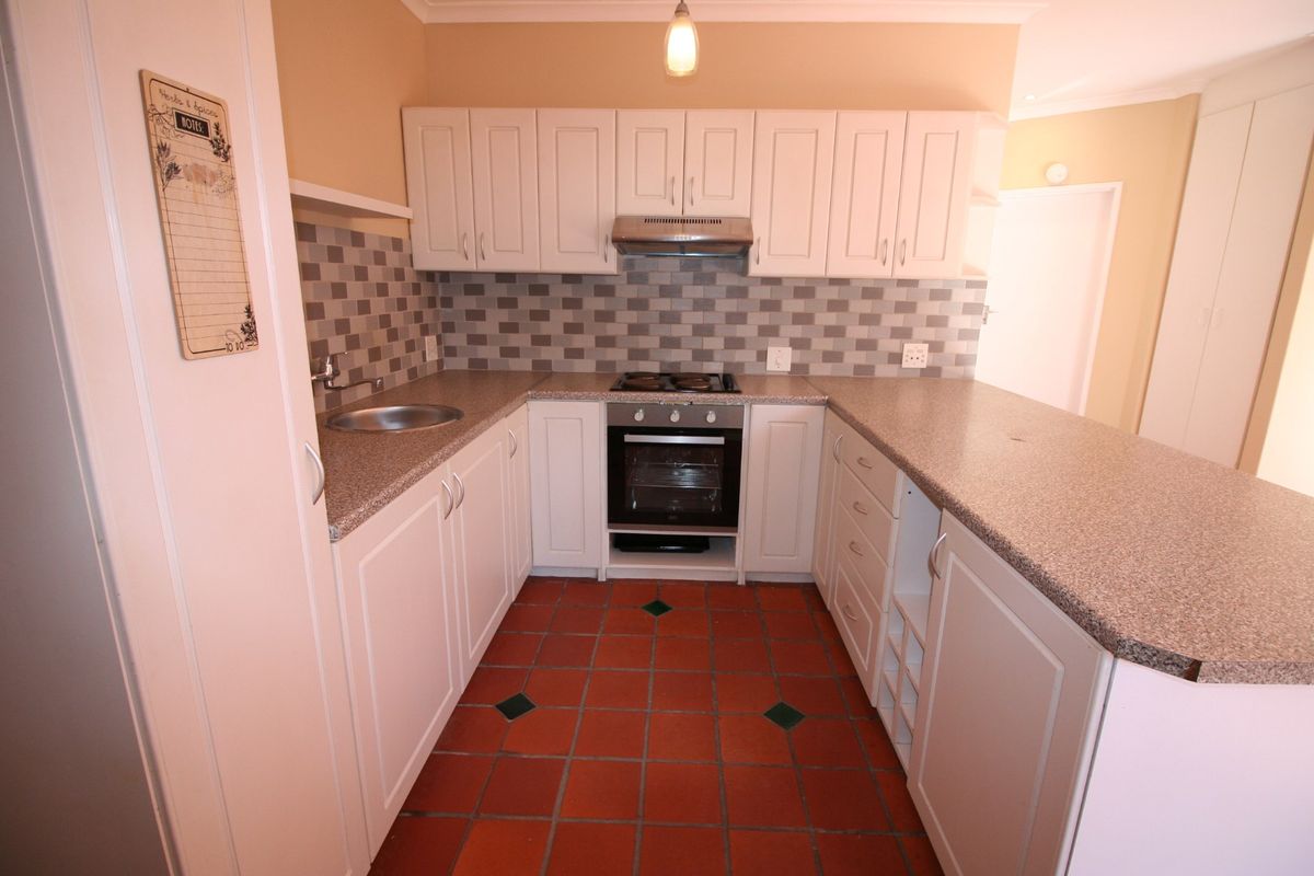 A functional kitchen featuring white cabinetry, granite-look laminate countertops, a built-in oven with hob, and traditional terracotta floor tiles.