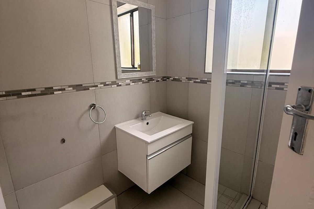 A compact, modern bathroom featuring a wall-mounted vanity, a glass-enclosed shower, and neutral ceramic tiling throughout.