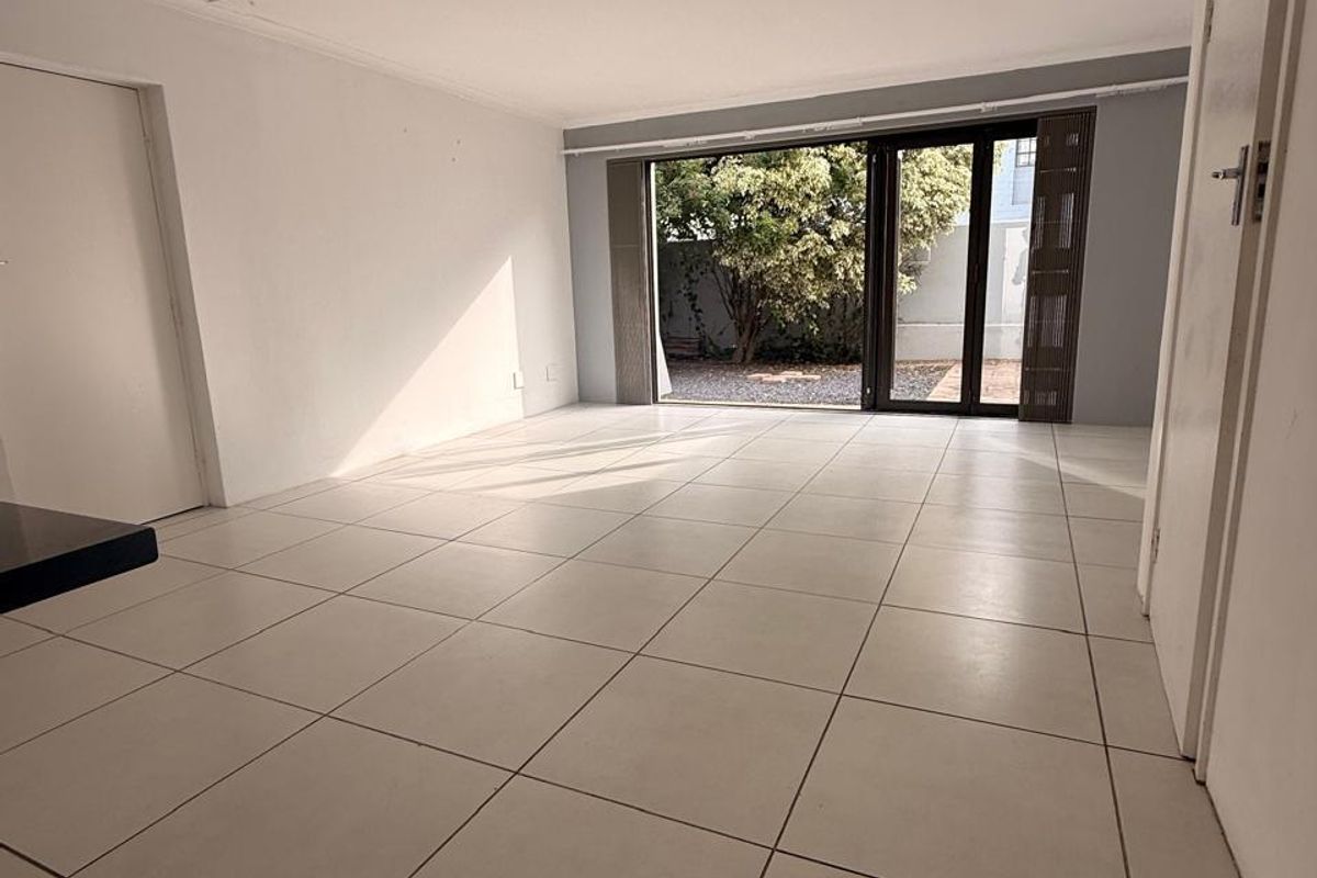 A bright, empty living room featuring neutral tiled flooring and a large sliding glass door providing direct access to the rear garden area.