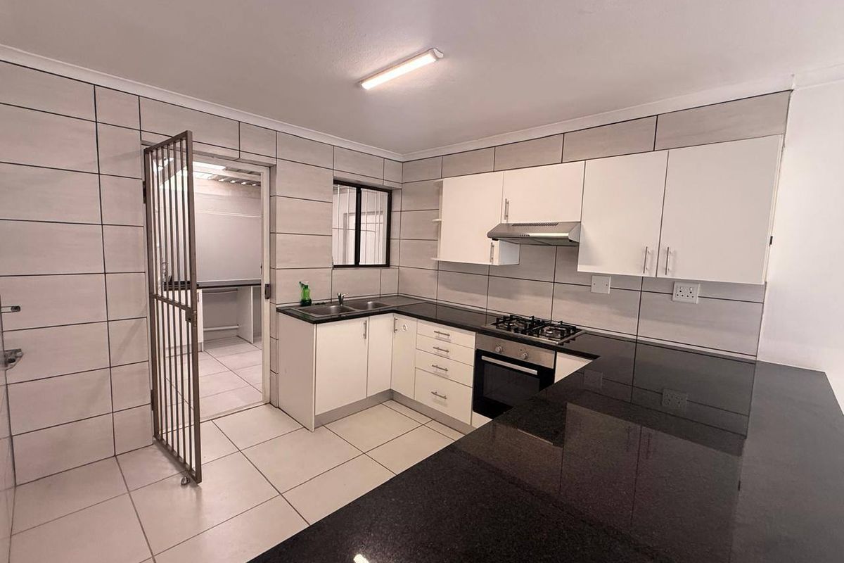 Modern kitchen featuring granite countertops, built-in gas hob, oven, extractor fan, and ample cabinetry, with an adjacent scullery area accessible via a security gate.