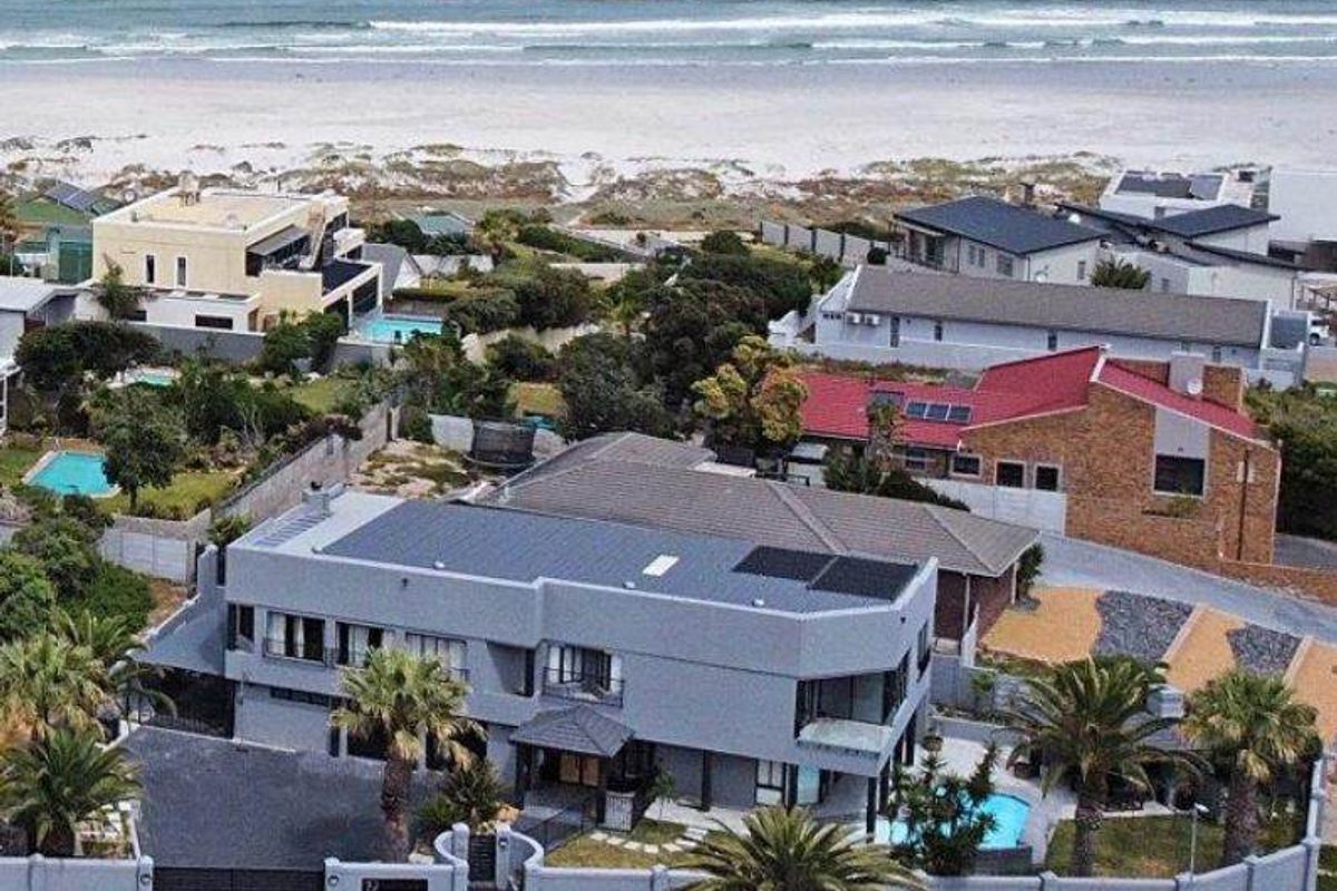 Aerial view of a coastal property featuring a swimming pool, solar panels, and a secure gated entrance, situated near the beach.
