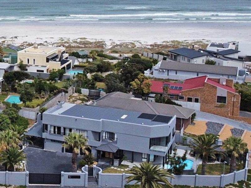 Aerial view of a coastal property featuring a swimming pool, solar panels, and a secure gated entrance, situated near the beach.