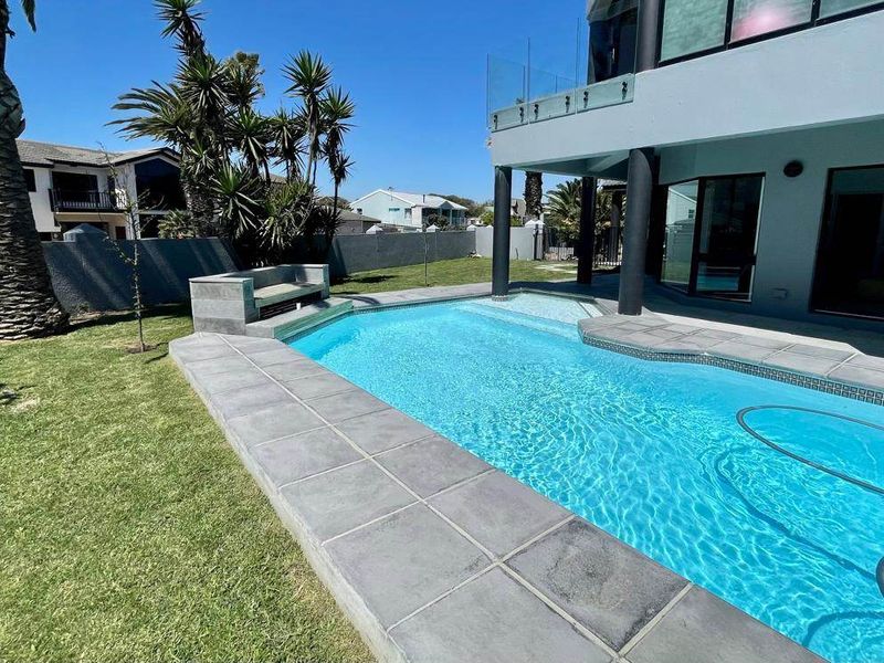A well-maintained swimming pool area featuring stone coping, a built-in stone bench, and a glass balustrade, set within a landscaped garden.
