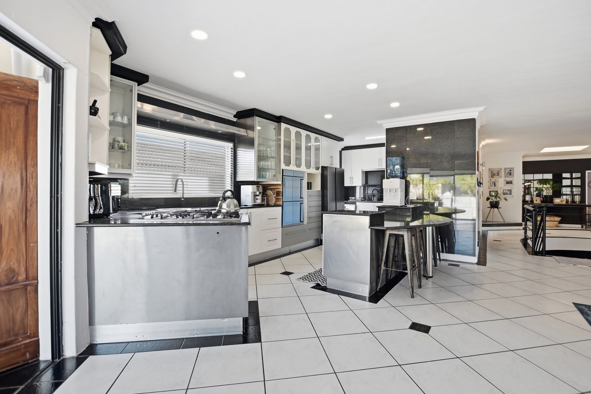 Modern kitchen featuring stainless steel cabinetry, granite countertops, built-in oven, gas cooktop, and tiled flooring with a spacious open-plan layout.