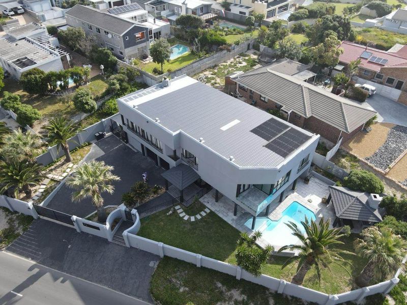 Aerial view of a modern residential property featuring a swimming pool, solar panels, paved driveway, and well-maintained garden areas.