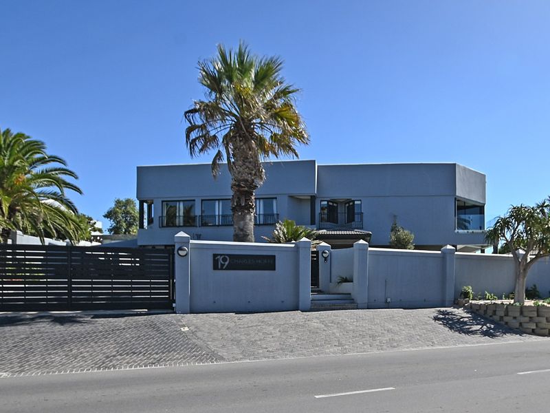Front elevation of a modern multi-story house featuring a paved driveway, secure boundary wall, and balcony access.