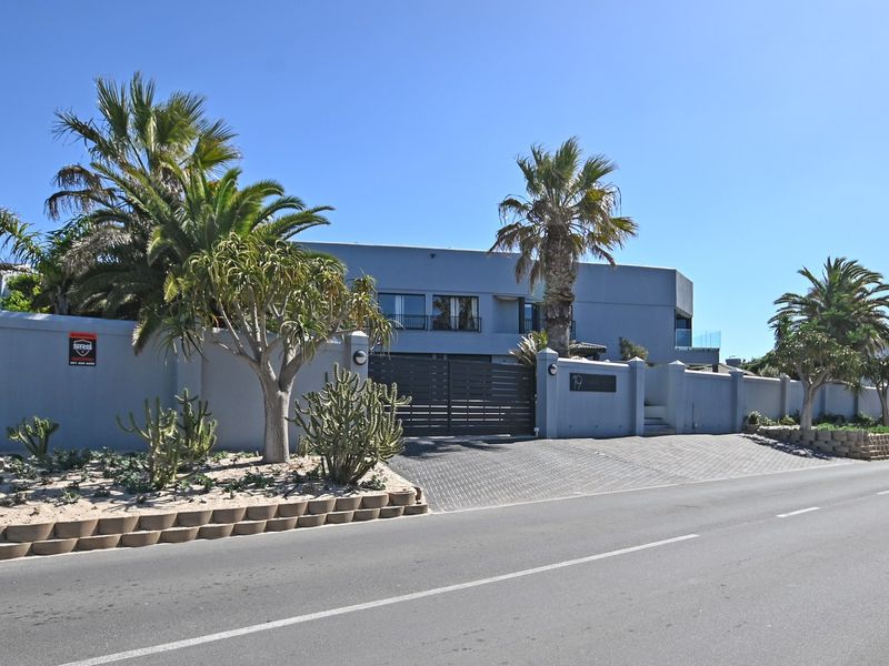 Front elevation of a modern residence featuring a secure boundary wall, paved driveway, and gated entrance with established landscaping.