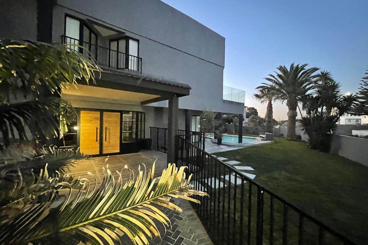 Rear view of a modern two-story house featuring a covered patio, balcony with glass balustrade, swimming pool, and a well-maintained garden.