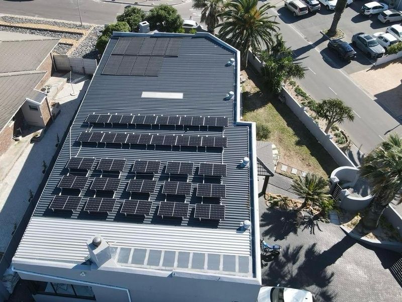 Aerial view of the property showing a large roof installation of solar panels, a skylight, and the surrounding paved driveway and landscaping.