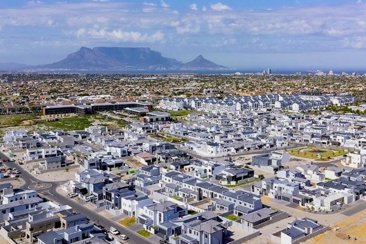 An aerial view of a modern residential estate with paved roads, showcasing the surrounding neighbourhood and distant mountain landscape.