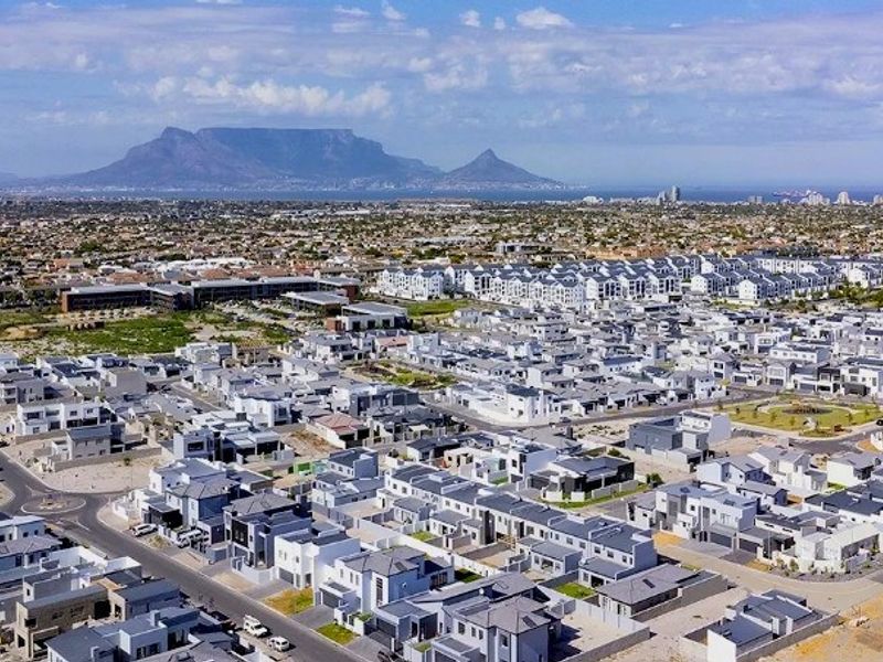 An aerial view of a modern residential estate with paved roads, showcasing the surrounding neighbourhood and distant mountain landscape.