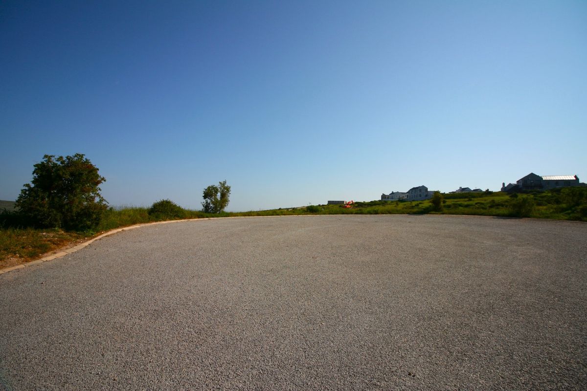 A view of a gravel road surface and surrounding landscape in a residential area.