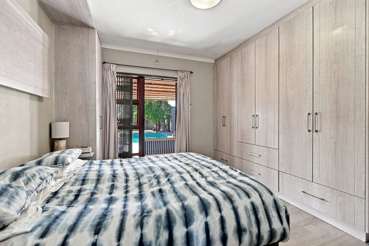 A well-maintained bedroom featuring extensive built-in cupboards and a sliding door providing direct access to the outdoor pool area.
