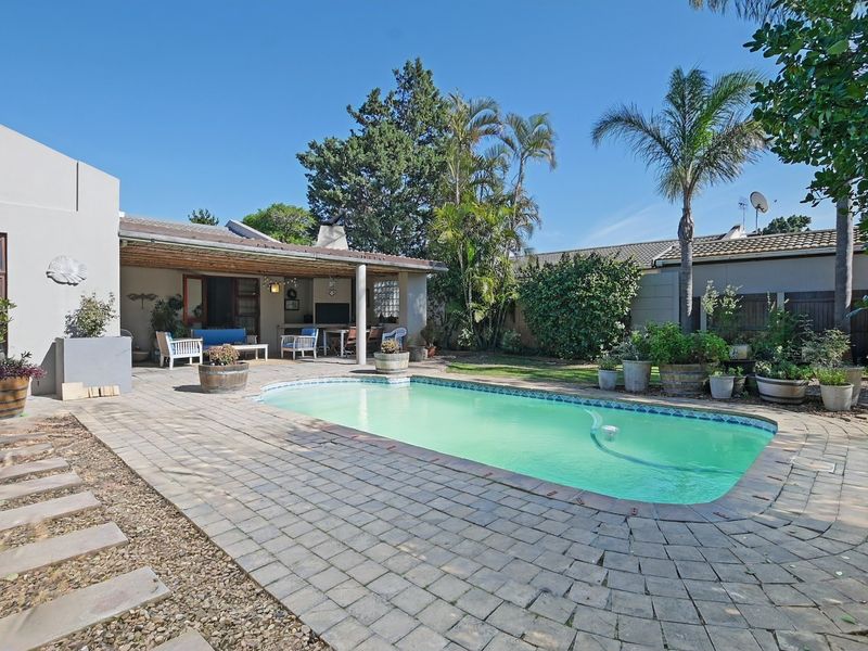 A well-maintained outdoor entertainment area featuring a swimming pool, paved patio, and a covered patio with a built-in braai.