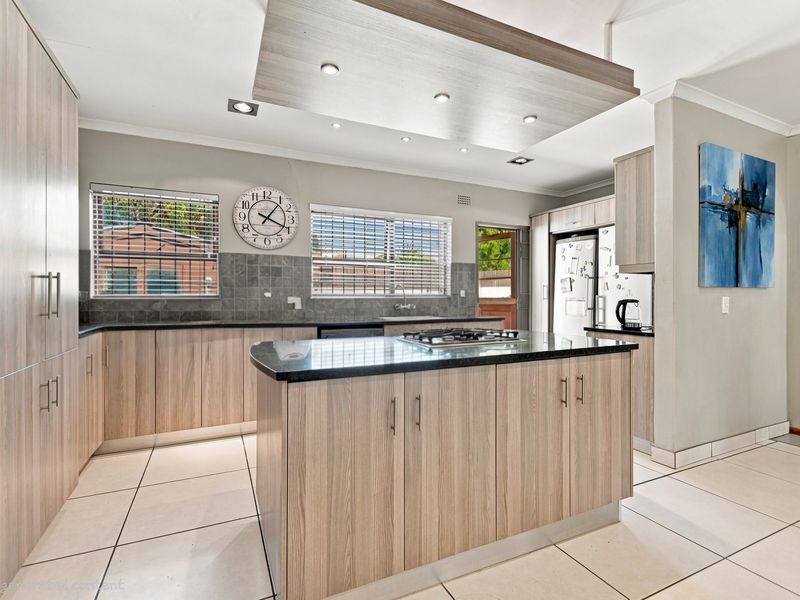 Modern kitchen featuring light wood-grain cabinetry, a central island with a gas cooktop, stone countertops, and recessed lighting throughout.