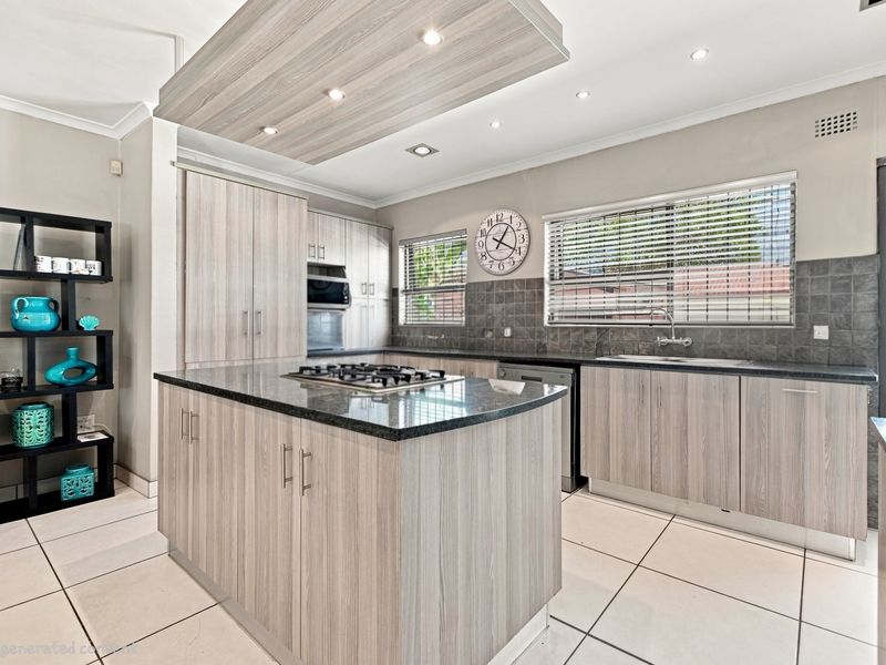 Modern kitchen featuring light wood-grain cabinetry, a central island with a gas cooktop, stone countertops, and a tiled backsplash with recessed lighting.
