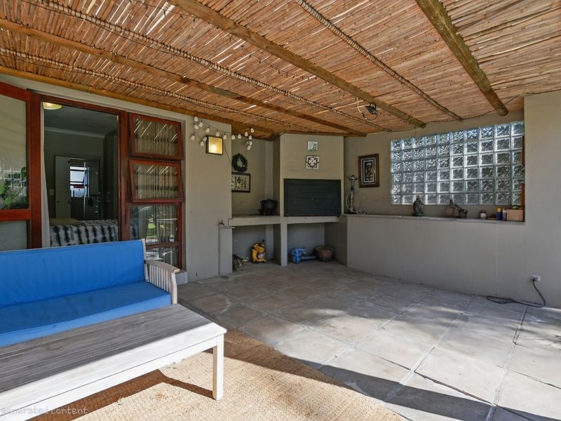Covered outdoor patio featuring a built-in braai, tiled flooring, and a rustic thatched roof, providing a functional space for outdoor entertaining.