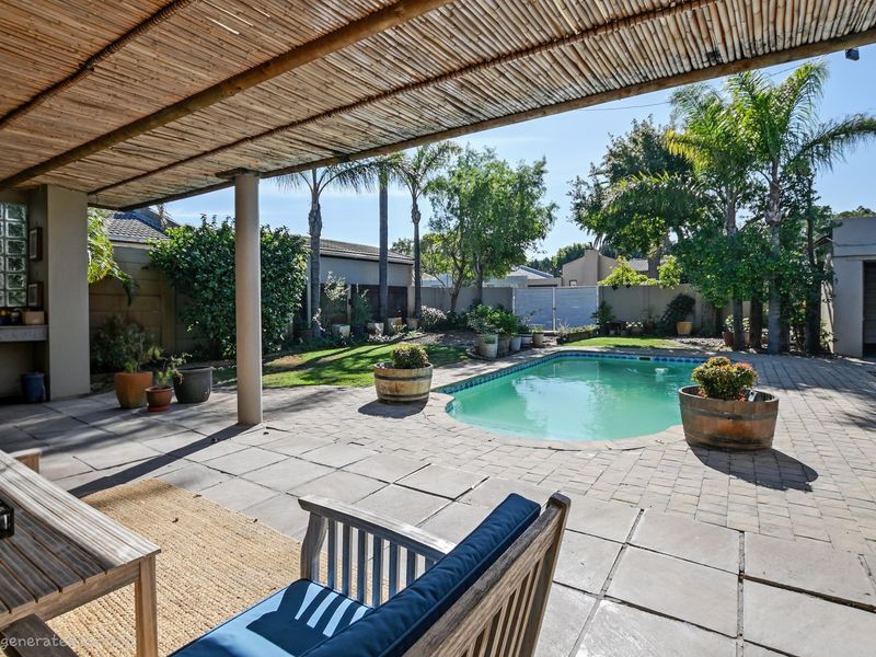 Outdoor entertainment area featuring a paved patio, swimming pool, and a covered bamboo pergola, overlooking a landscaped garden.