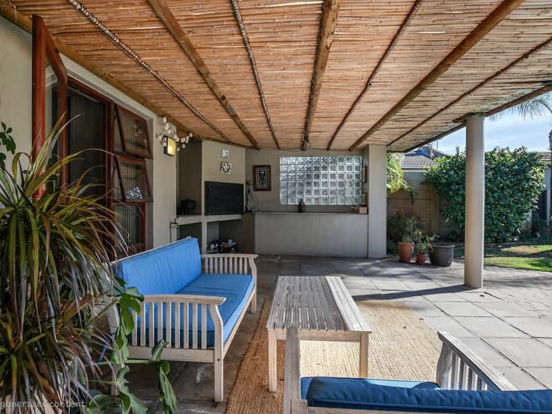 Covered outdoor patio featuring a bamboo ceiling, built-in braai area, and glass block feature wall, overlooking the garden.