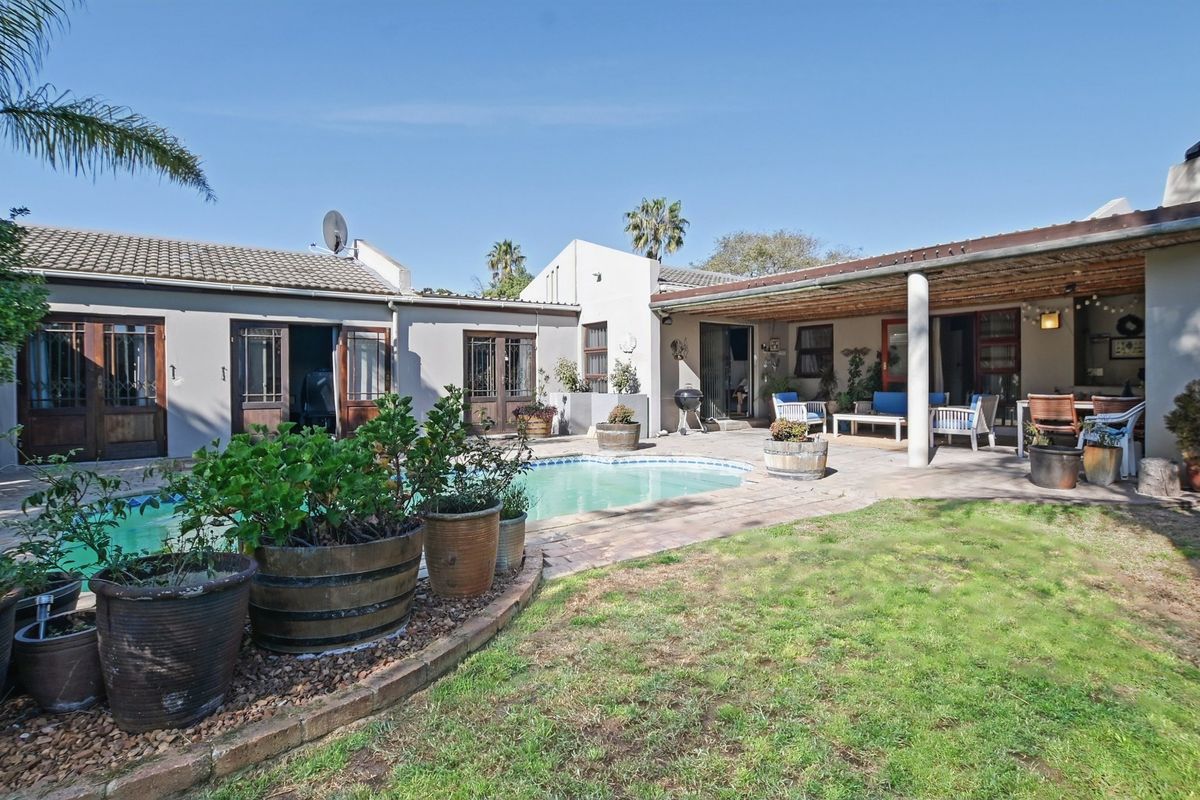 Rear exterior view featuring a swimming pool, covered patio area, and established garden space with paved surrounds.