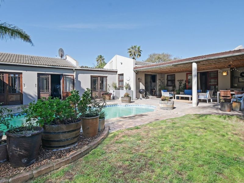 Rear exterior view featuring a swimming pool, covered patio area, and established garden space with paved surrounds.