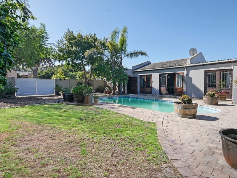 A private backyard featuring a swimming pool, paved patio area, and established garden with boundary walling.
