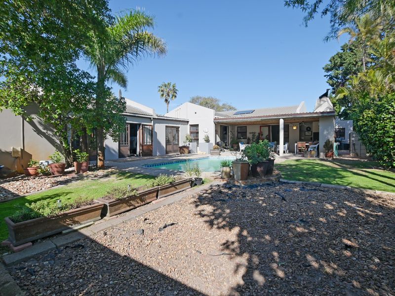 Rear view of the property featuring a swimming pool, covered patio with an outdoor fireplace, and a landscaped garden area.