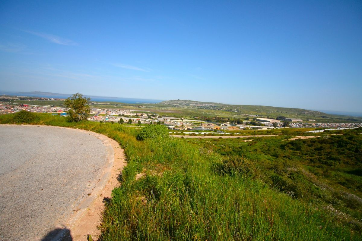 Elevated panoramic view overlooking the surrounding landscape, residential area, and distant coastline from a paved access road.