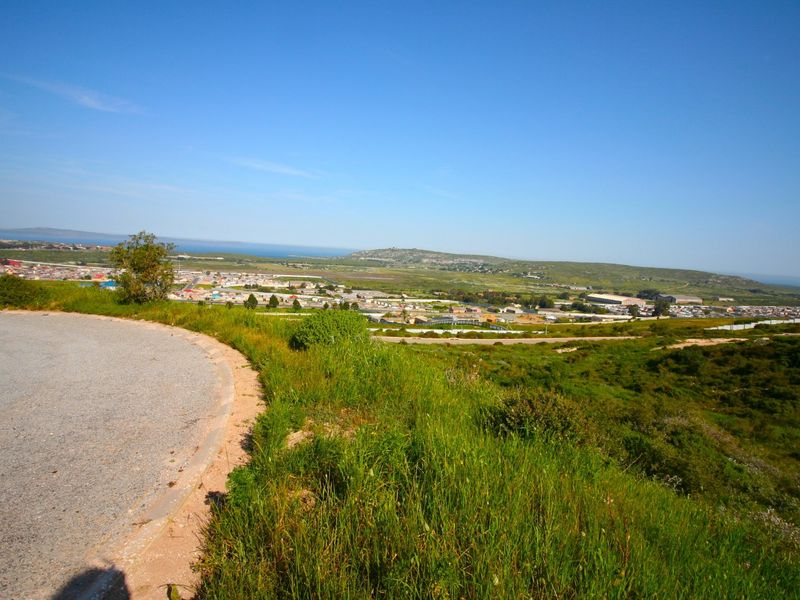 Elevated panoramic view overlooking the surrounding landscape, residential area, and distant coastline from a paved access road.