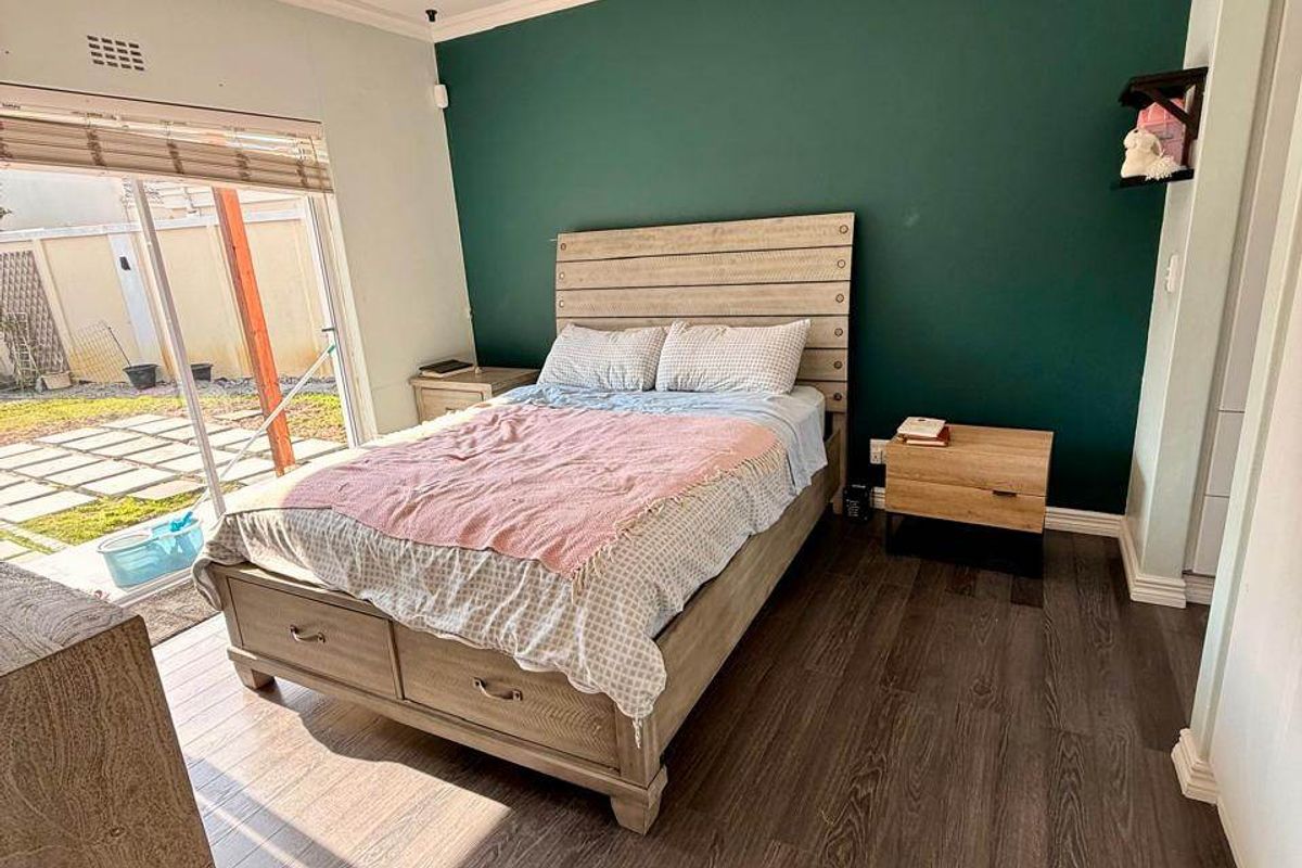 A well-lit bedroom featuring dark laminate flooring, a bold green accent wall, and a sliding glass door providing direct access to the outdoor patio area.