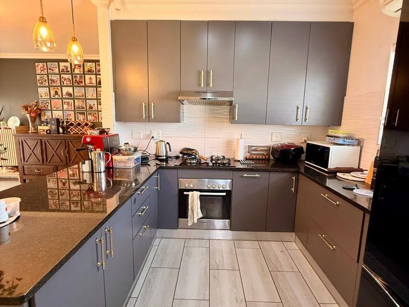 Modern kitchen featuring dark grey cabinetry, granite countertops, built-in oven, gas hob, and stylish recessed ceiling lighting with neutral tiled flooring.