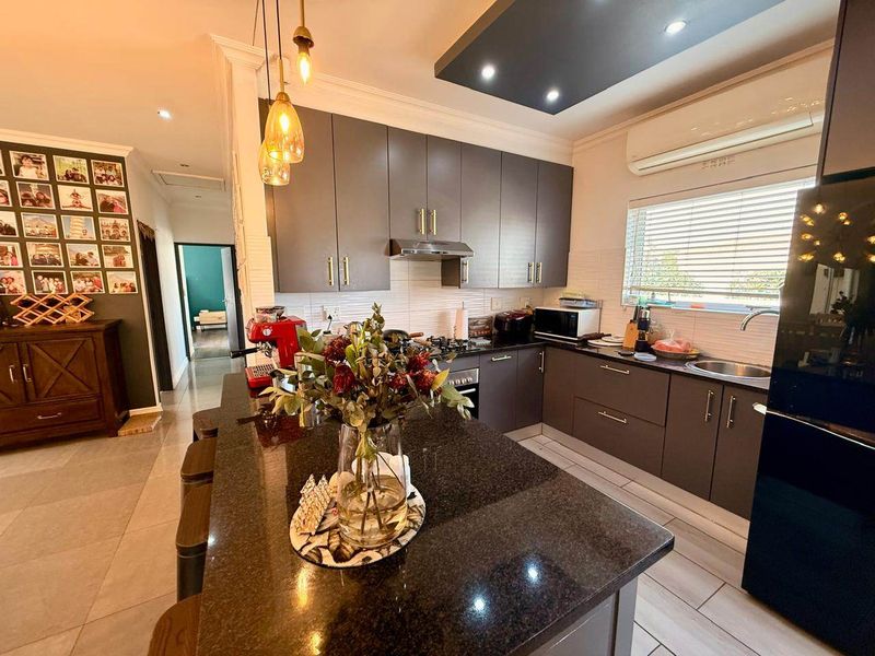 Modern kitchen featuring dark cabinetry, granite countertops, a central island, and integrated appliances, complemented by recessed lighting and tiled flooring.